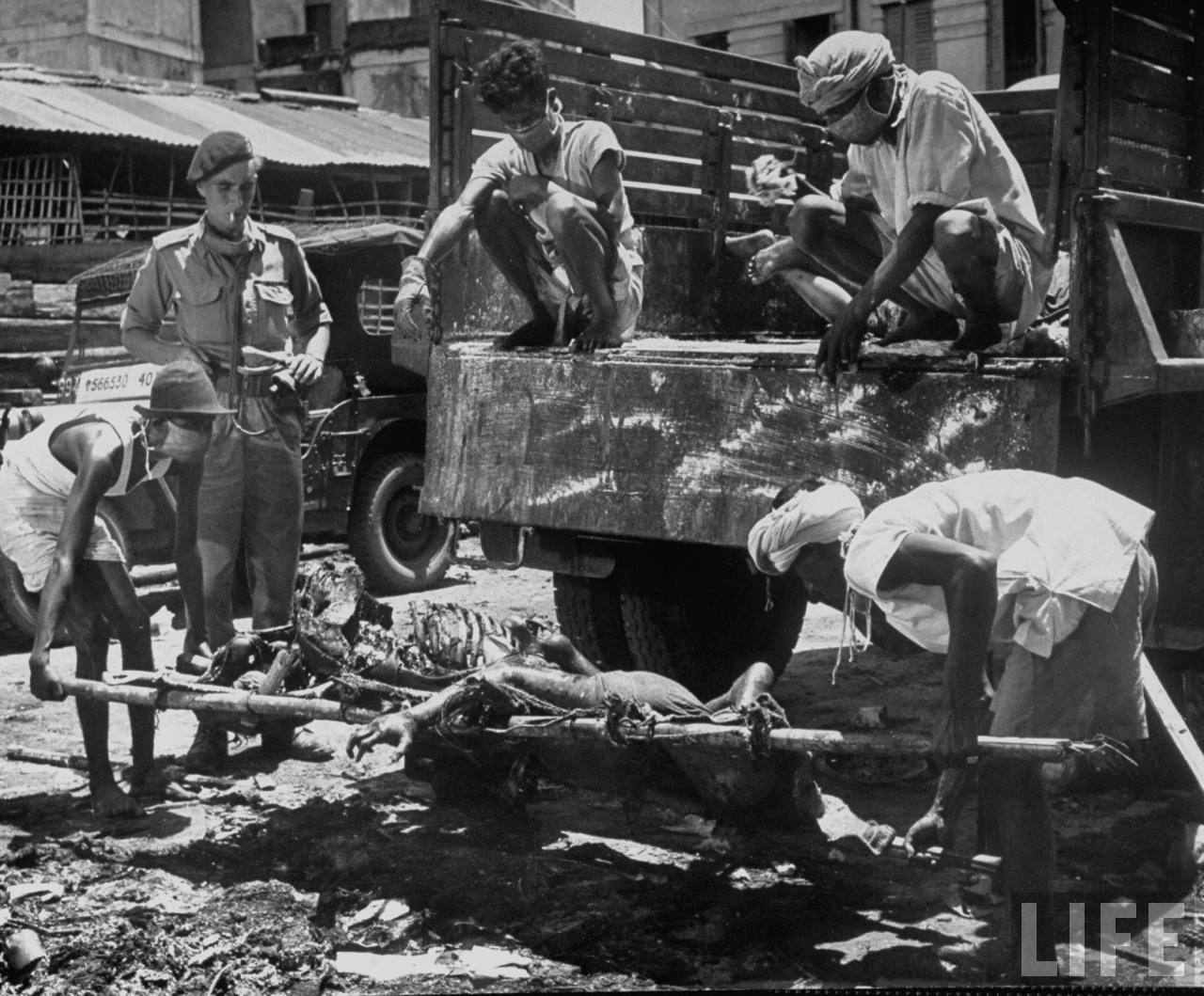 Men unloading corpses from truck in preparation for cremation